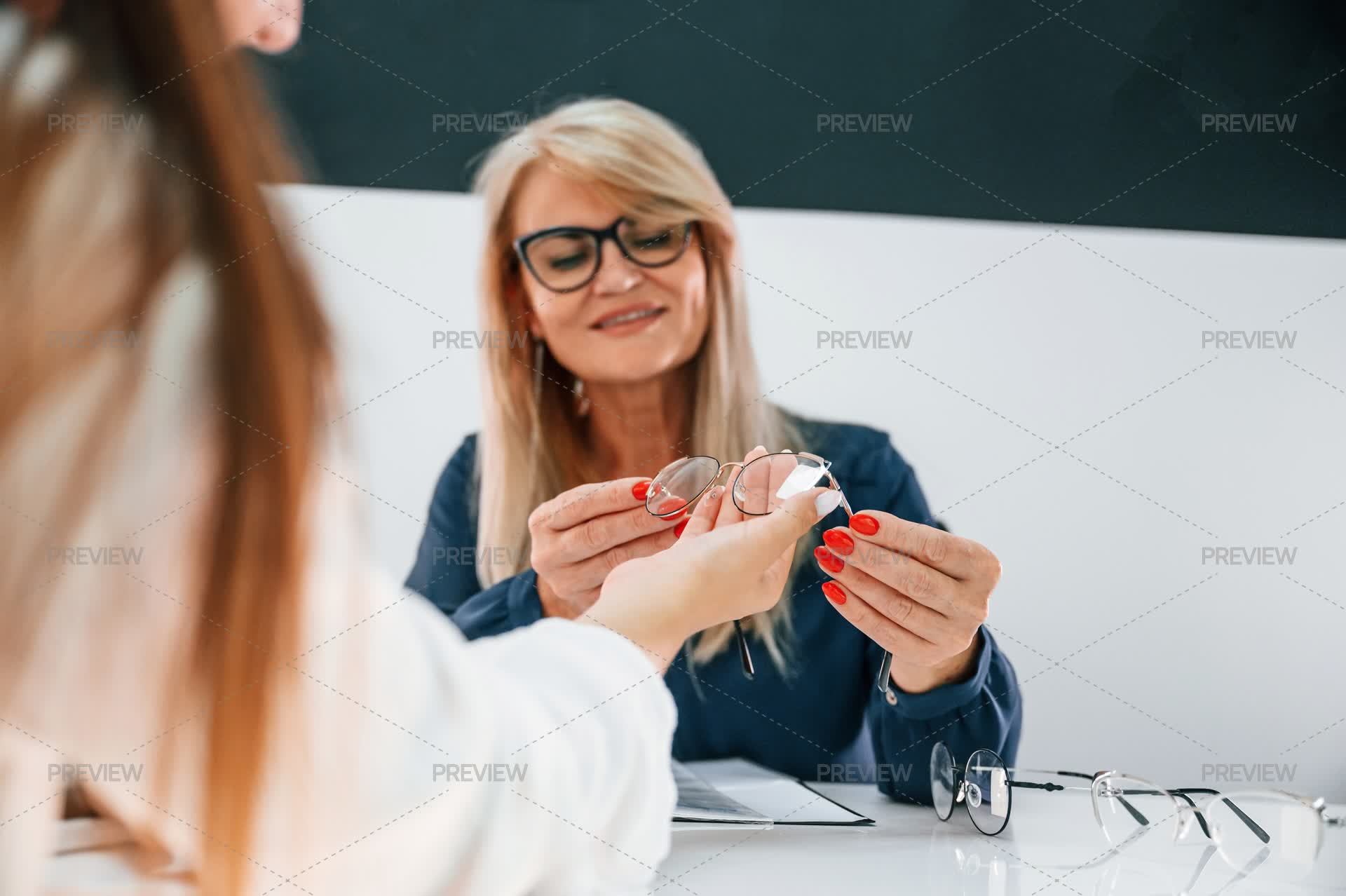 Woman Choosing Glasses In The Store And Getting Help From Assistant ...