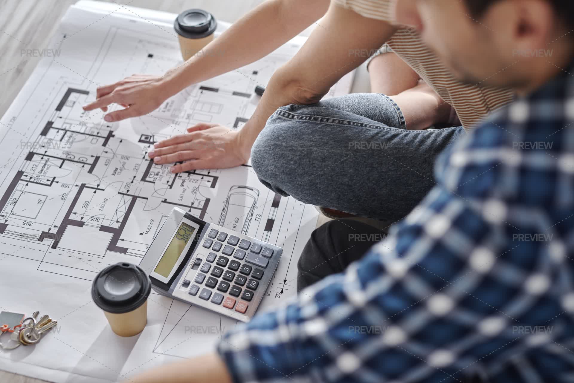 Couple Calculating Renovation Costs Using Floor Plan And Calculator by ...